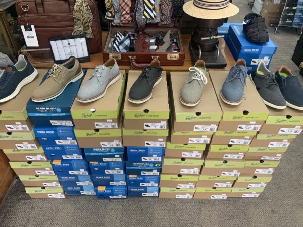 Display of Nunn Bush and Florsheim canvas shoes atop stacked shoe boxes with accessories in the background.